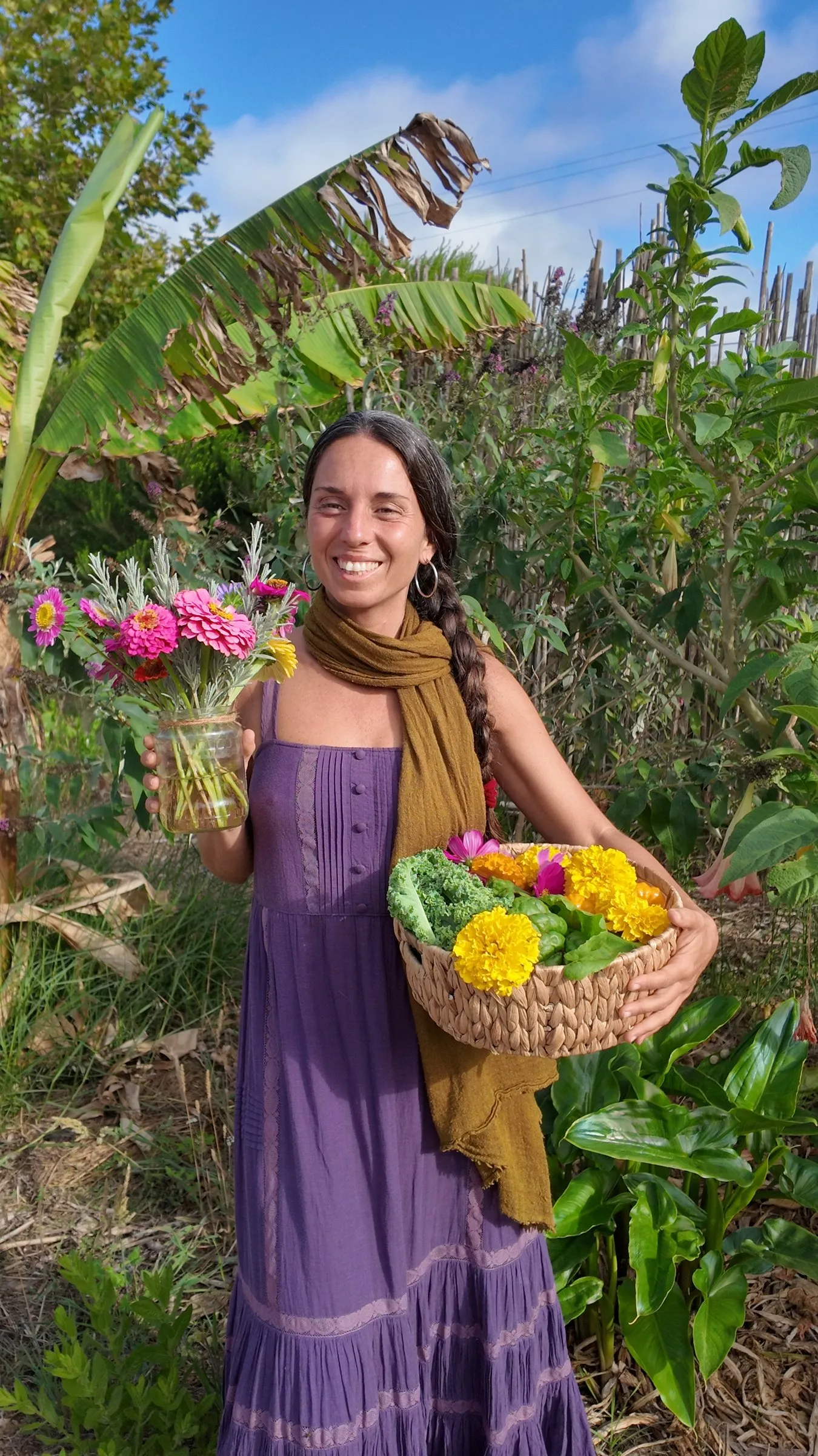 Melania smiling in the garden with a jar of zinnias and a basket of marigolds and kale